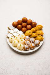 Indian sweets in a plate includes Gulab Jamun, Rasgulla, kaju katli, morichoor / Bundi Laddu, Gujiya or Karanji for diwali celebration