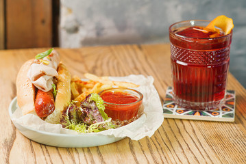 old fashioned cocktail and plate with hot dog with sausage and ham, tomato sauce ketchup and french fried on the table in the bar