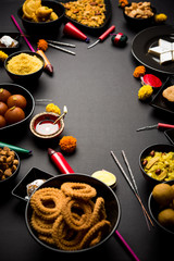 Diwali sweets and snacks arranged in a group with Diya or oil lamp, flowers and Fire Crackers or Patakhe over moody background, selective focus