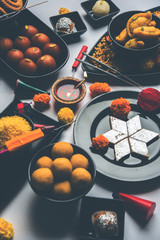 Diwali sweets and snacks arranged in a group with Diya or oil lamp, flowers and Fire Crackers or Patakhe over moody background, selective focus