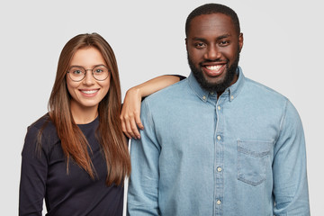 Horizontal shot of mixed race couple stand closely to each other, being in good mood, collaborate...