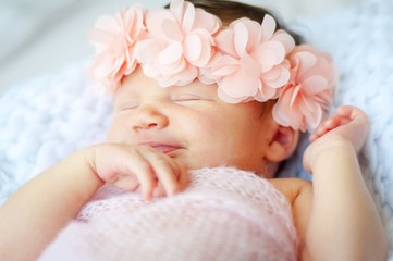 Cute and adorable Caucasian newborn baby girl with a pink flower head band smiling in her sleep.