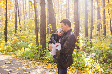 Fatherhood, family and leisure concept - father holding little daughter in his arms in autumn park