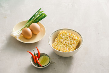 Instant noodles in bowl and vegetable side dishes on stone background. Quick & easy food concept.