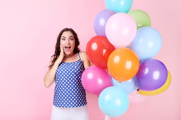 Fototapeta na wymiar Surprised girl with colored balloons on pink background