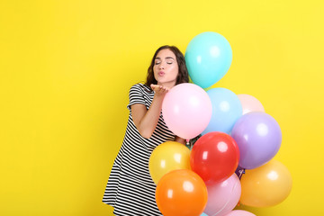 Fototapeta na wymiar Cute girl with colored balloons on yellow background