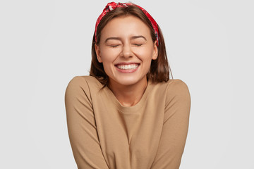 Portrait of happy European woman has broad smile, closes eyes, feels excitement, being in high...