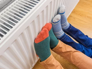 Foto op Aluminium Woman and child wearing colorful pair of woolly socks warming cold feet in front of heating radiator in winter time. Electric or gas heater at home. © Evgen