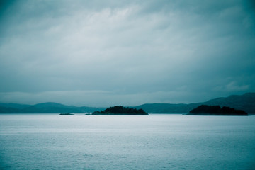 Fototapeta premium A dramatic, overcast scenery on the coeast of fjord during a ferry ride in Norway near Bergen. Moody autumn landscape of fjord.
