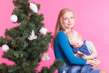 Christmas and holiday concept - Portrait of smiling woman with her little daughter decorating Christmas tree over pink background