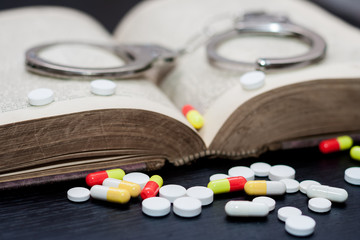 Handcuffs and pills and drugs on wooden table