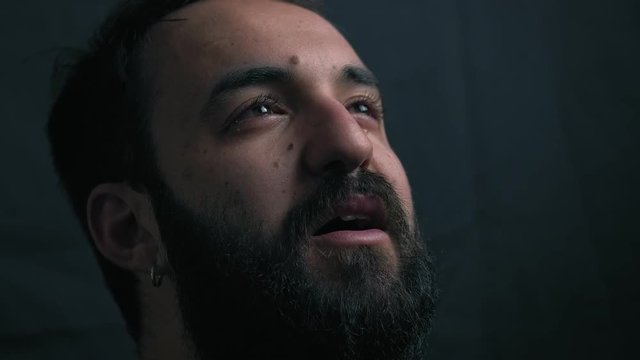 close up portrait of young bearded man crying and praying in the darkness