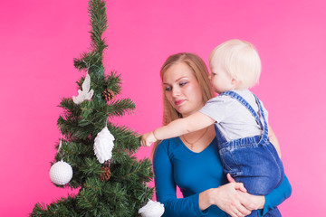 Christmas, holidays and people concept - woman and her kid near christmas tree over pink background