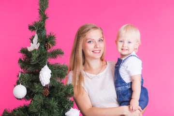 Holidays and people concept - Woman and her kid near christmas tree on pink background