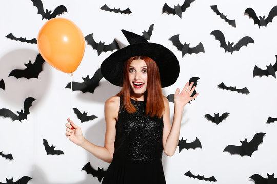 Beautiful redhaired woman with balloons and paper bats on white background