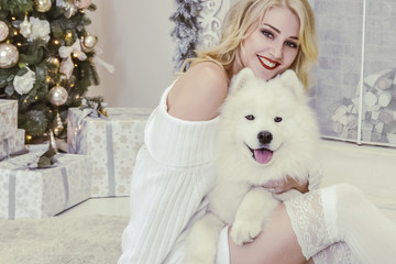 beautiful blonde in white clothes with a white husky on the background of the fireplace and Christmas tree.