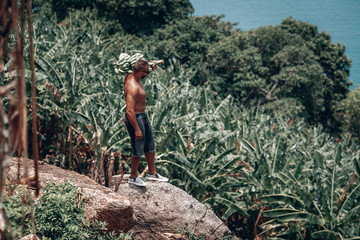 sports Guy in the jungle with a beautiful view of the sea in the hands of a large bunch of bananas . Thailand, Phuket island