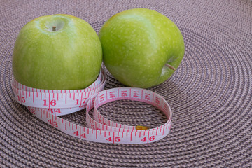 Measuring tape wrapped around a green apple as a symbol of diet.