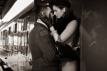 Vintage couple embracing on railway station platform as train is about to depart
