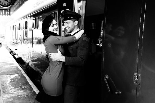 Vintage couple embracing and laughing on railway station platform as train arrives