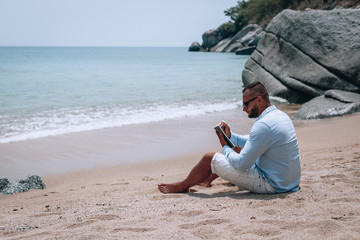 a young businessman in sunglasses, blue shirt and shorts writes in a notebook