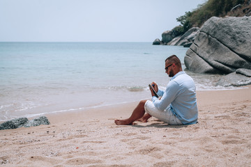 a young businessman in sunglasses, blue shirt and shorts writes in a notebook