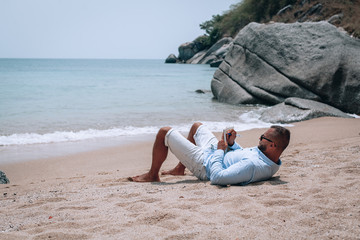 a young businessman in sunglasses, blue shirt and shorts writes in a notebook