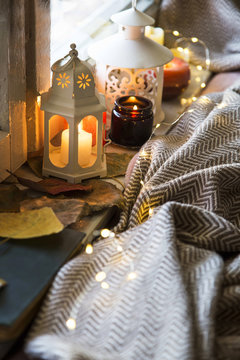 Cozy festive autumn decor still life, fall still life candles and lanterns at window with lights and blanket