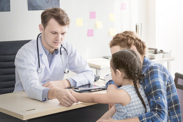 Fototapeta premium Pediatrician (doctor) man examining,reassuring and discussing child at surgery .Mother Caucasian and kid smiling in hospital room.Copy space.