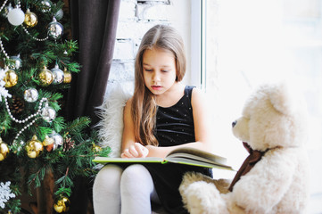 girl reading fairy tales on the window, near the Christmas tree,