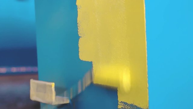 Man is painting large blue metal detail by hand roller to yellow color. Painter at the factory. Professional workshop. Heavy industry servis and metal construction factory