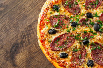 Pizza with Mozzarella cheese, salami, pepper, pepperoni, olives, Spices and Fresh Basil. Italian pizza on wooden background