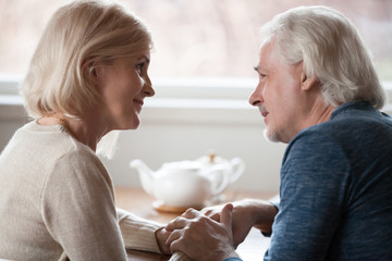 Happy loving senior middle aged retired family couple holding hands looking in the eyes giving care psychological support to older, understanding in good relations, trust devotion in marriage concept