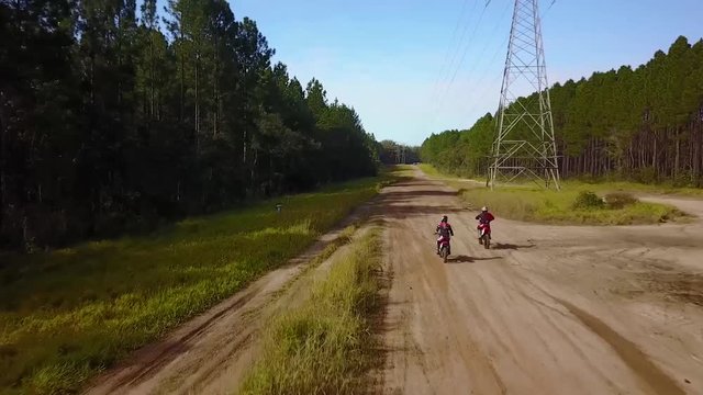 Aerial tracking drone shot following off-road motorcycles or dirt bikes, racing on a sand road, in a forest, at Glass house mountains national park, in Queensland, Australia