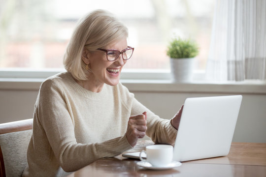 Happy Mature Middle Aged Elderly Business Woman Winner Excited By Reading Good News Looking At Laptop, Glad Senior Older Lady Watching Celebrating Online Bid Bet Win Or Great Result Victory Concept