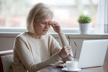 Upset fatigued overworked senior mature business woman taking off glasses tired of computer work,...