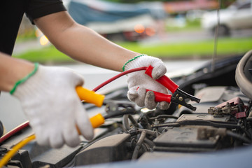 Fototapeta premium Young man charging battery car with electricity trough jumper cables on the country road, insurance and service concept.