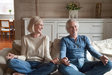 Mature couple having fun laughing doing yoga together at home, happy middle aged family sitting in...