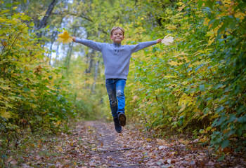 happy European boy runs and jumps on the path in autumn Park