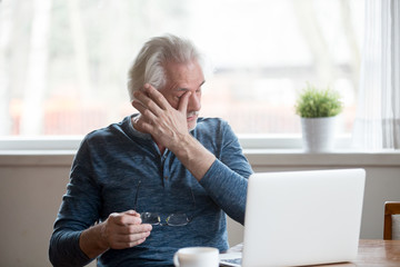Fatigued mature old man taking off glasses suffering from tired dry irritated eyes after long...
