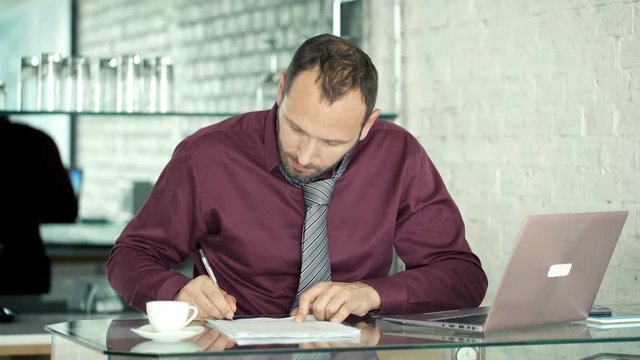 Businessman signing documents sitting by table in the office, 4K
