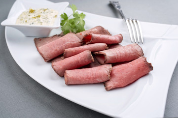 Traditioneller deutscher Brotzeit Aufschnitt mit Roastbeef Scheiben und Remulade  als closeup auf einem weißem Teller