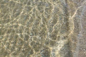 texture d'acqua marina e piccole onde in superficie su sfondo di sabbia e conchiglie spezzate