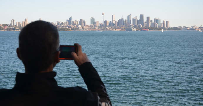 Man takes photos of Sydney panorama with his mobilephone. View of Sydney skyline and Sydney Harbour from Nielsen Park.