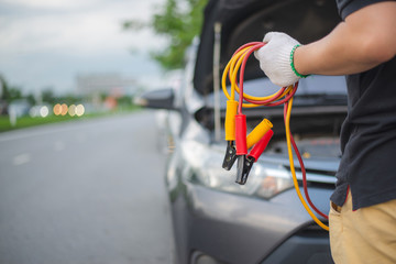 Young man charging battery car with electricity trough jumper cables on the country road,copy...