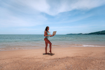 Young successful business woman or student in swimsuit  using laptop in the beach. Working outdoors on seescape background. Mobile Office concept