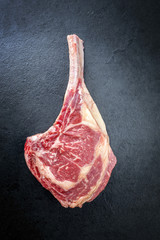 Rohes dry aged Wagyu Tomahawk Steak als Draufsicht auf einem schwarzen Board mit Textfreiraum