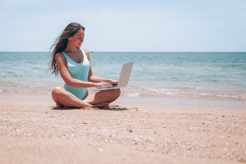 Fototapeta premium beautiful and sexy young woman sitting in lotus pose and medetiruet on a lounger with a laptop by the sea. woman freelancer doing yoga with a laptop in the beach resort