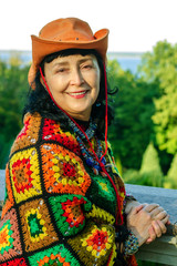 Elegant attractive senior woman in bright multi colored clothes and an orange hat is at nature in autumn park. Vertical.