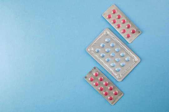 Blister packs of blue and pink pills on blue background with copyspace